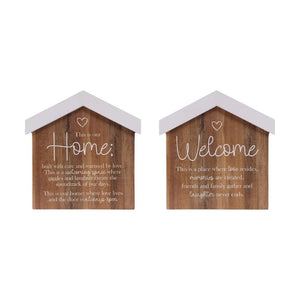 Two small house-shaped wooden wall signs with white roofs and white script text, shown side by side on a plain white background. One sign says "Home" and the other says "Welcome by Saddle & Bloom.