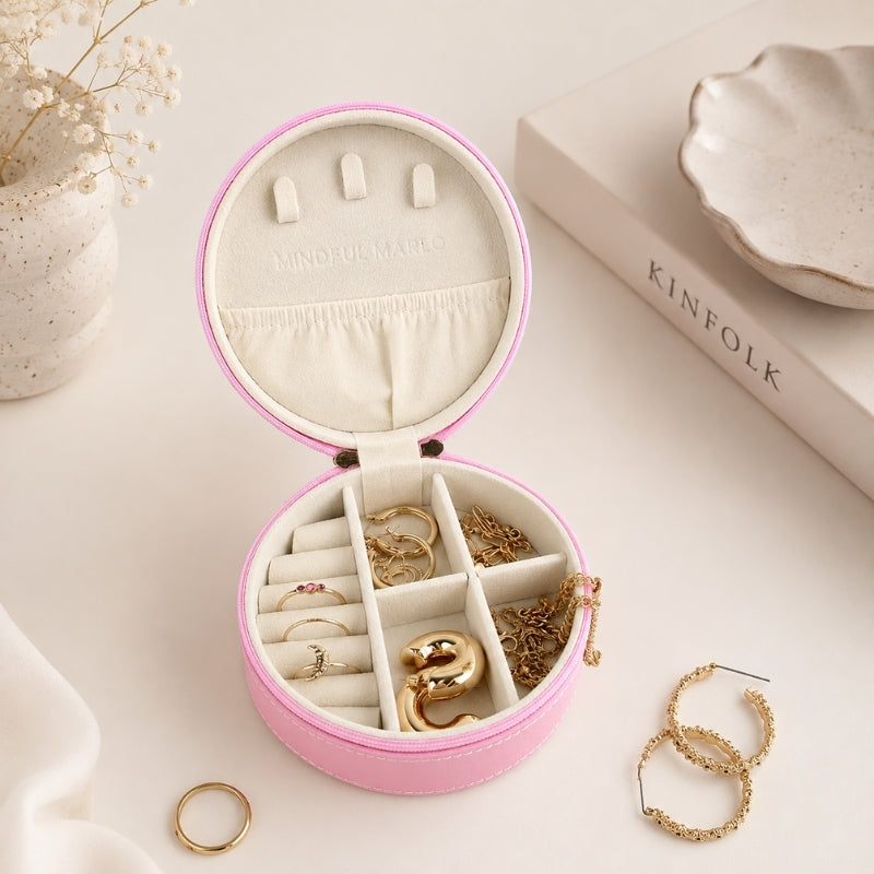 A Small Jewellery Case – Berry is shown open on a light cream surface, containing several rings and bracelets. The box has a pink exterior, cream interior, and small ring slots on the lid.
