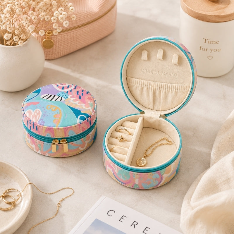 Two Small Jewellery Cases – Haven with a colorful abstract pattern in pink, blue, and beige, displayed on a light marble surface. One box is closed, and the other is open to show its cream-colored interior with ring slots and small pouches, styled with gold jewelry and decorative props.