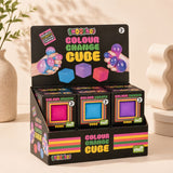 A retail display box containing three boxes of SMOOHOO Colour Change Cube toys, arranged on a beige tabletop with decorative ceramic vases in the background.