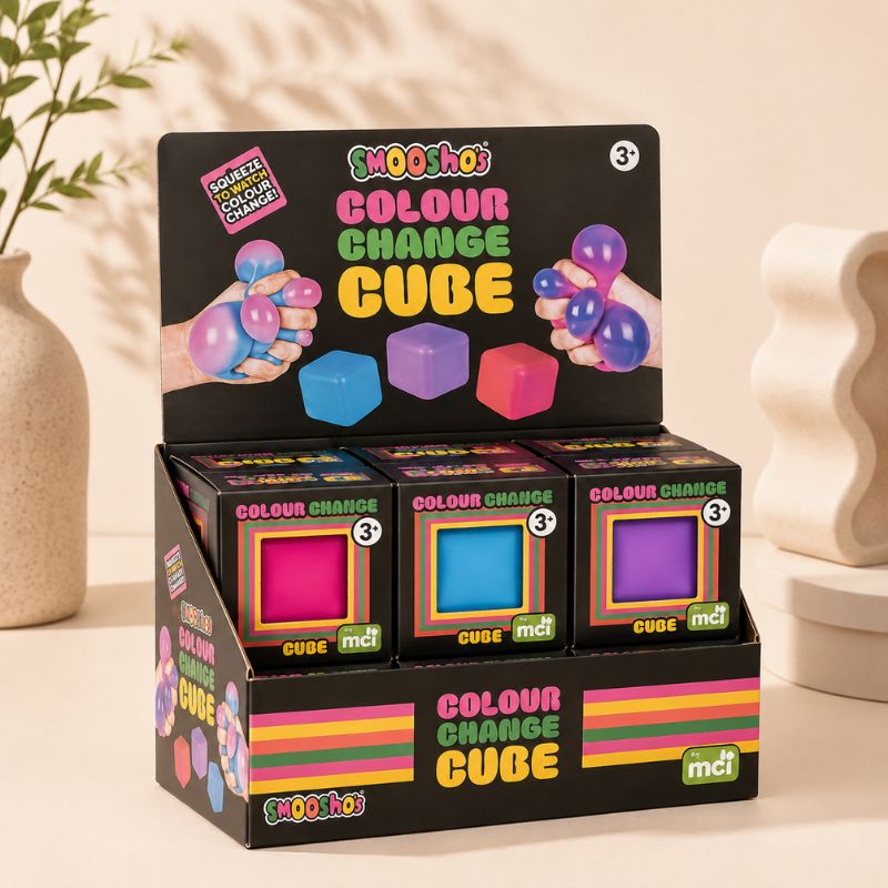 A retail display box containing three boxes of SMOOHOO Colour Change Cube toys, arranged on a beige tabletop with decorative ceramic vases in the background.
