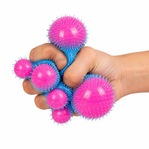 A hand gripping a cluster of pink and blue textured stress balls against a plain white background.