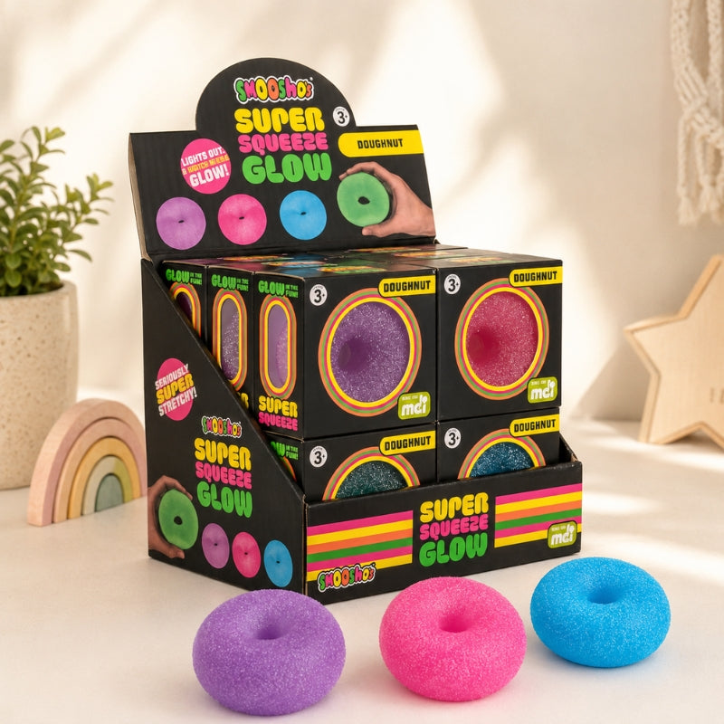 A retail display box of 'Bloomio' Super Squeeze Glow Doughnut candies, with three glow-in-the-dark doughnuts in purple, pink, and blue placed in front on a light-colored surface.