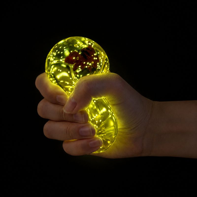 Close-up of a hand squeezing a glowing Smooshos Super Squeeze Diamond Sphere Dino stress toy