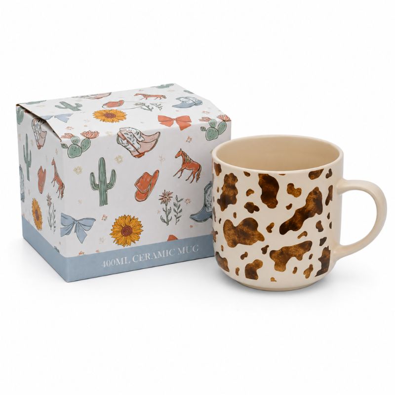 A 400ml Splosh - Saddle & Bloom Cow Mug on a cream background, shown next to its illustrated gift box on a white background.