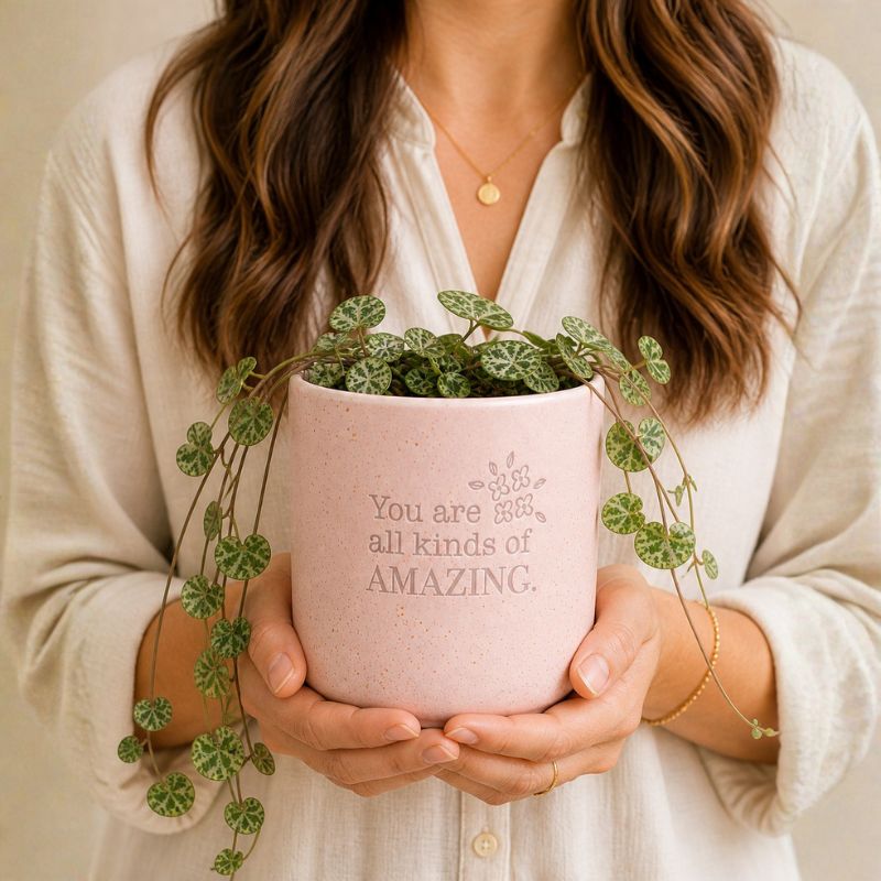 Woman holding pink inspirational ceramic planter with trailing green plant