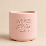Pink ceramic quote planter with “In the garden of life, friends are the flowers” on beige background