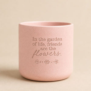 Pink ceramic quote planter with “In the garden of life, friends are the flowers” on beige background