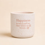 Neutral ceramic quote planter with “Happiness is the sunshine that helps us bloom” on beige background