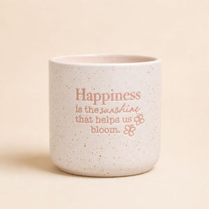 Neutral ceramic quote planter with “Happiness is the sunshine that helps us bloom” on beige background