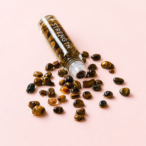 Glass roller bottle labeled 'STRENGTH' with tiger eye stones on a pink background