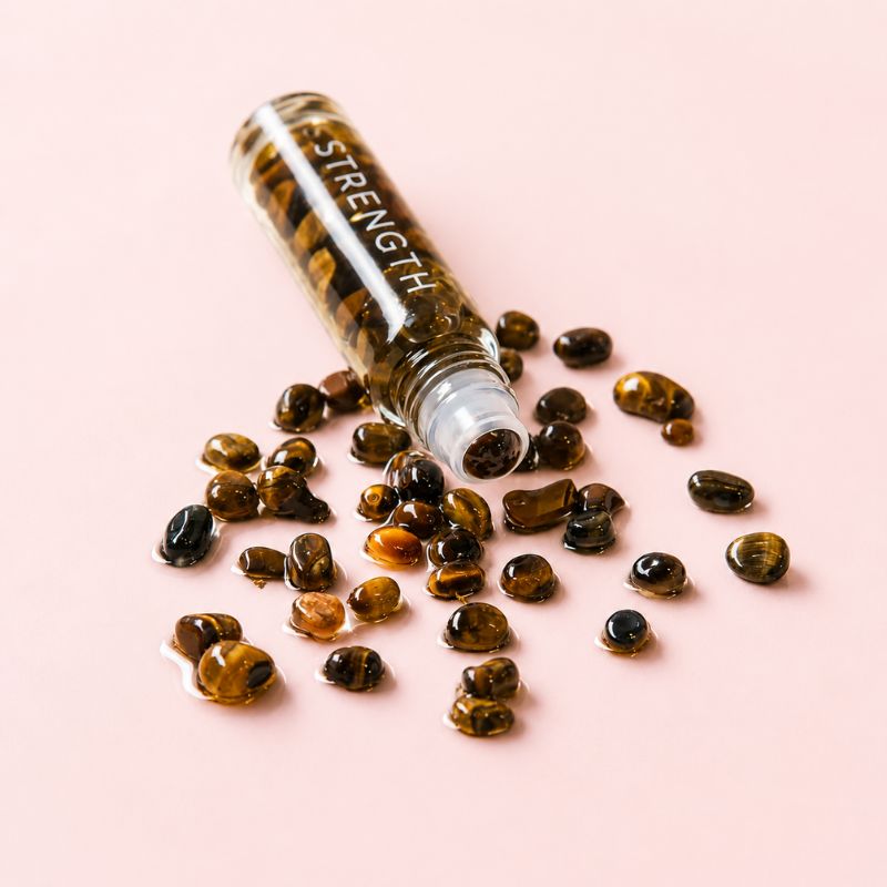 Glass roller bottle labeled 'STRENGTH' with tiger eye stones on a pink background