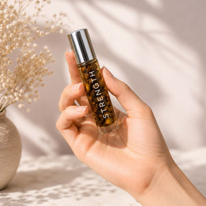 Hand holding a rollerball bottle labeled 'STRENGTH' with decorative elements in the background