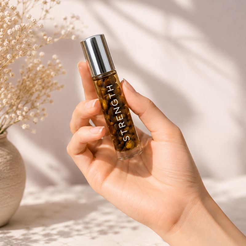 Hand holding a rollerball bottle labeled 'STRENGTH' with decorative elements in the background