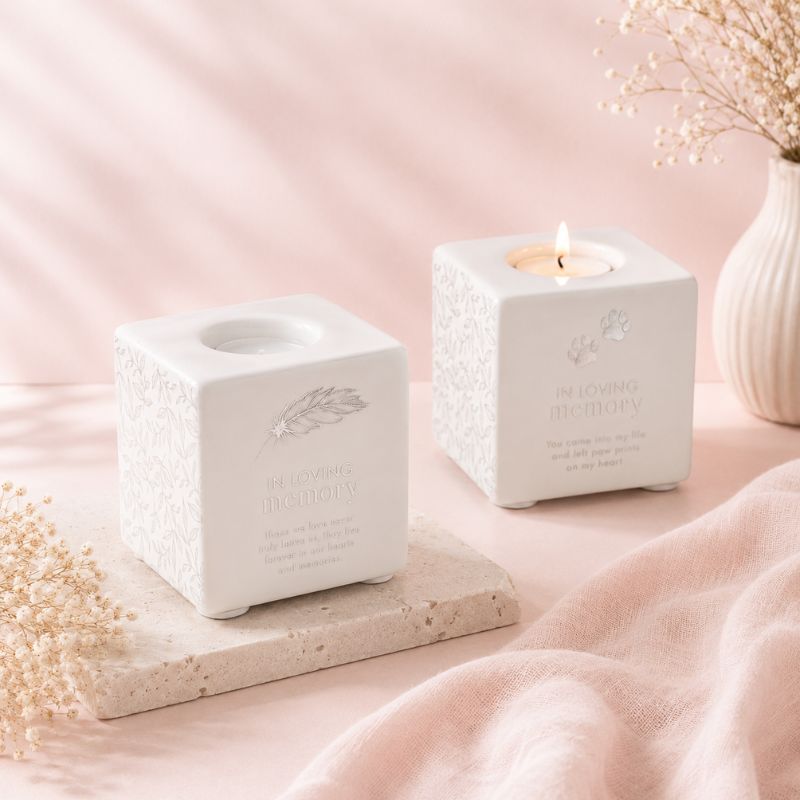Two white textured candle holders with engraved text on a pink surface.