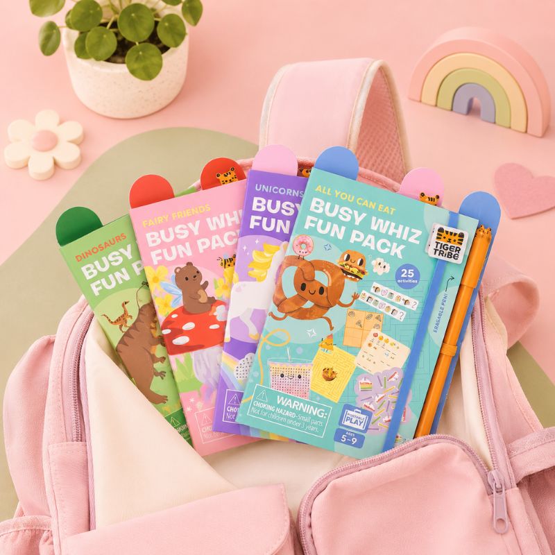Colorful 'Busy Whiz Fun Pack' books with pencils on a pink background
