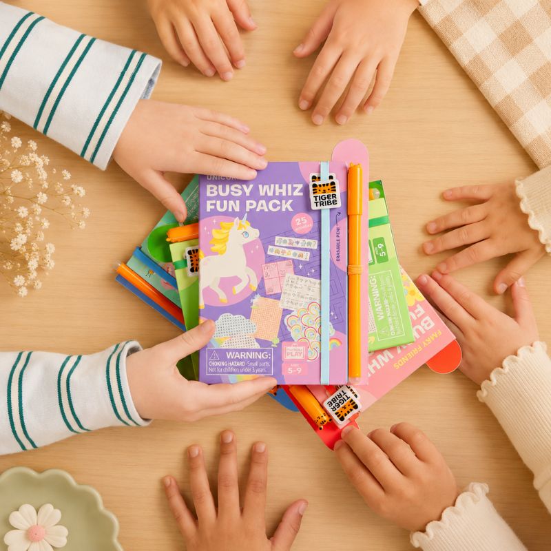 Children's hands around a Busy Whiz Fun Pack on a wooden table