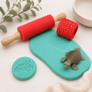 Teal fondant board with red embossing roller and turtle stamp, featuring 'wild dough' branding.