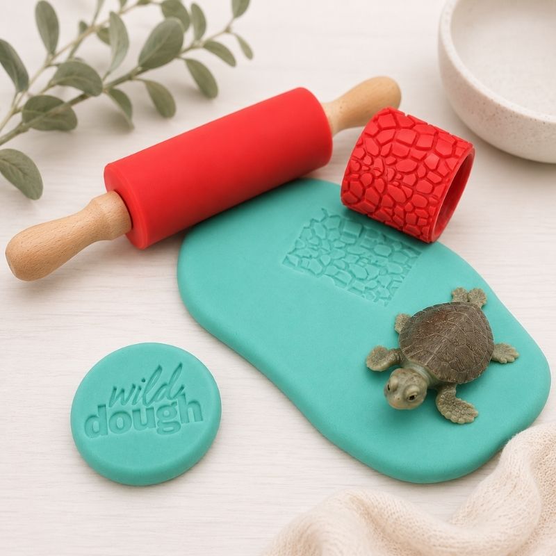 Teal fondant board with red embossing roller and turtle stamp, featuring 'wild dough' branding.