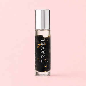 Small glass bottle labeled 'TRAVEL' with a silver cap on a pink background