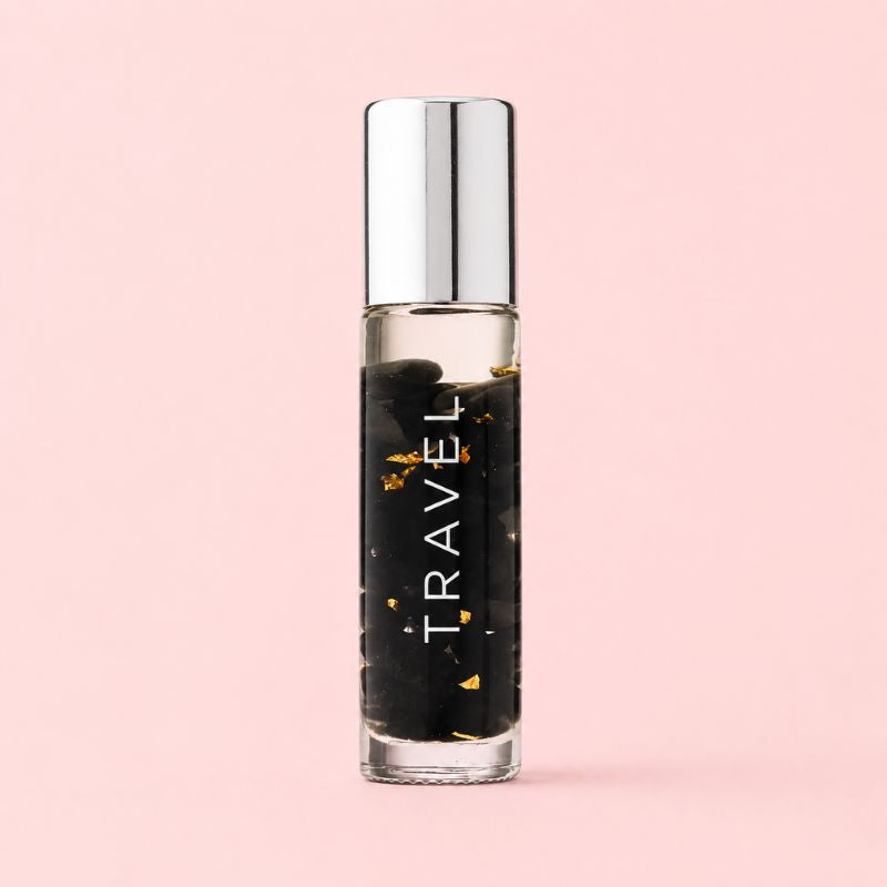 Small glass bottle labeled 'TRAVEL' with a silver cap on a pink background