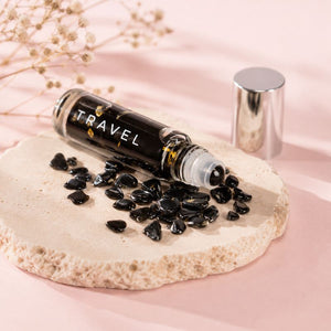 Roll-on bottle labeled 'TRAVEL' with black stones on a light pink background