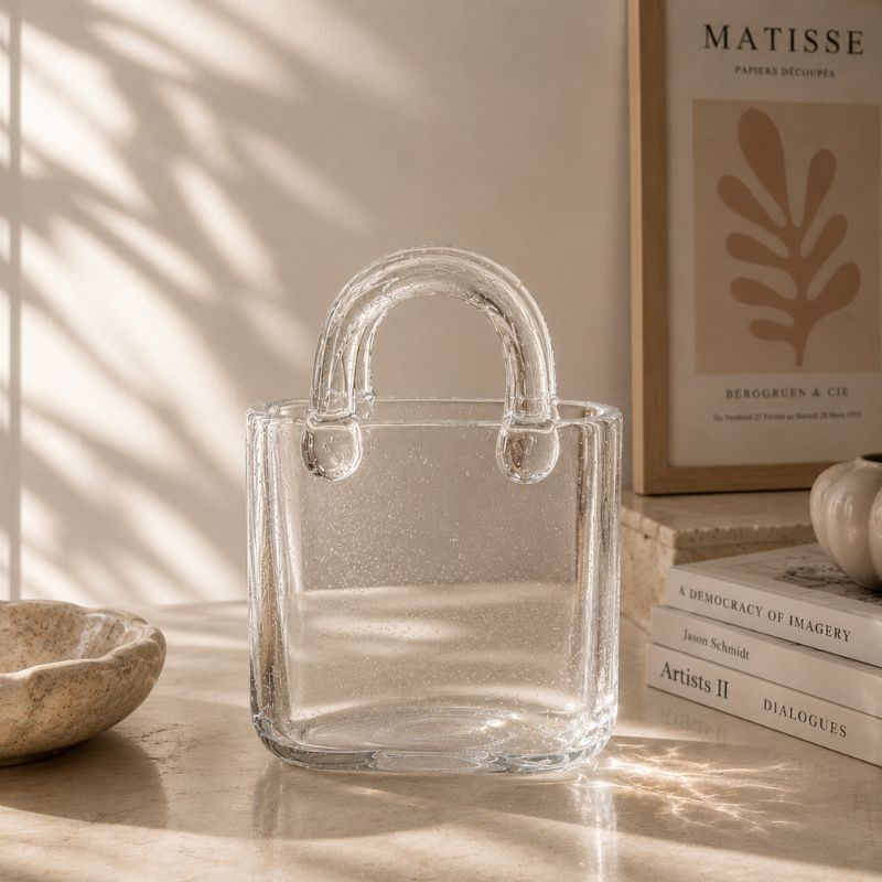 Clear glass handbag on a surface with books and decor in the background