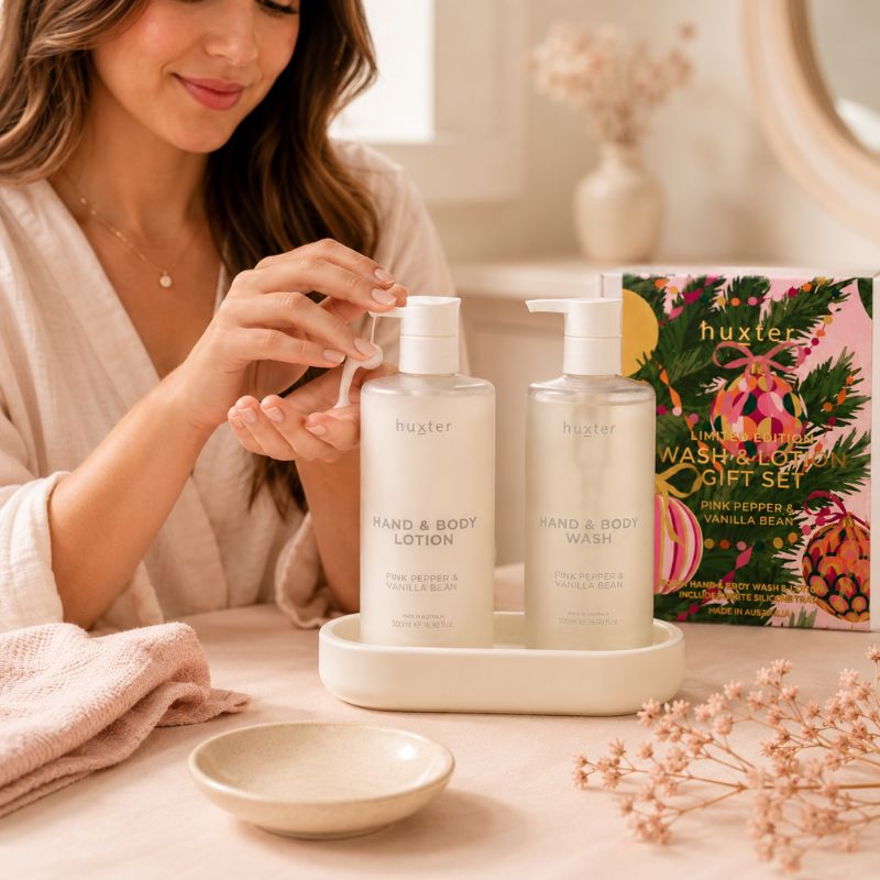 Woman using Huxter Pink Pepper & Vanilla Bean Hand and Body Lotion beside matching Wash and Lotion Gift Set
